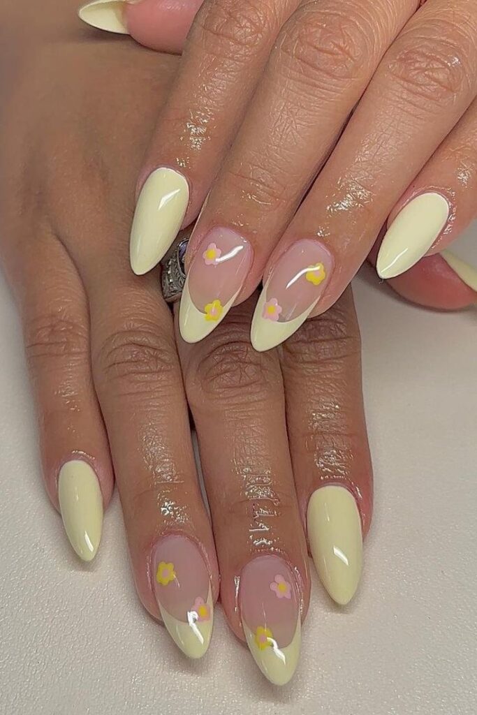 Image displays a set of hands with almond-shaped nails, featuring pastel yellow tips and delicate pink floral designs, evoking a summer garden feel.