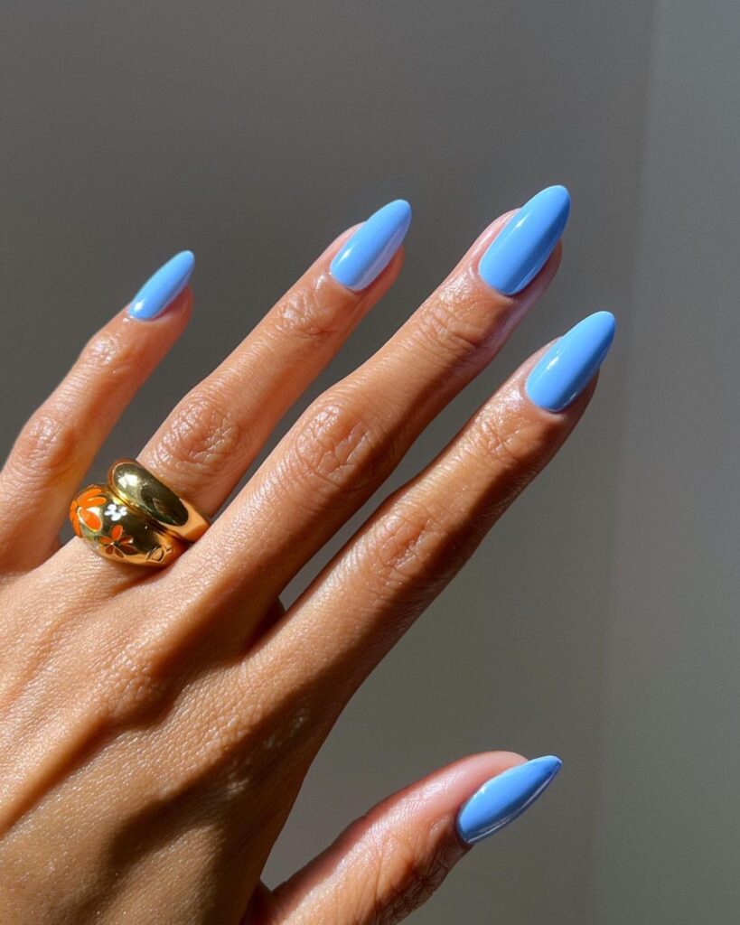 Photograph shows hands with long almond nails painted in a vibrant sky blue, complemented by a silver ring, capturing the essence of a perfect summer sky.