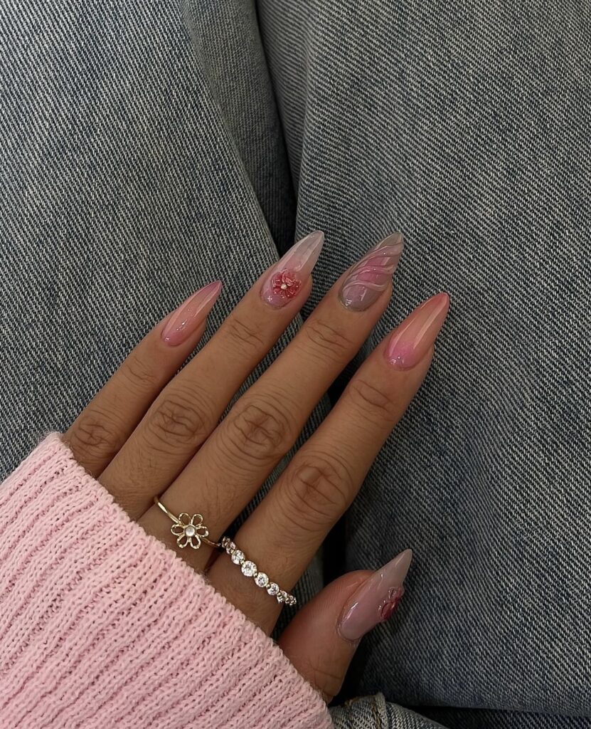 The photo shows hands with pointed nails, presenting a gradient of pink shades and delicate designs, adorned with glittering stones, inspired by the colors of a summer sunset.