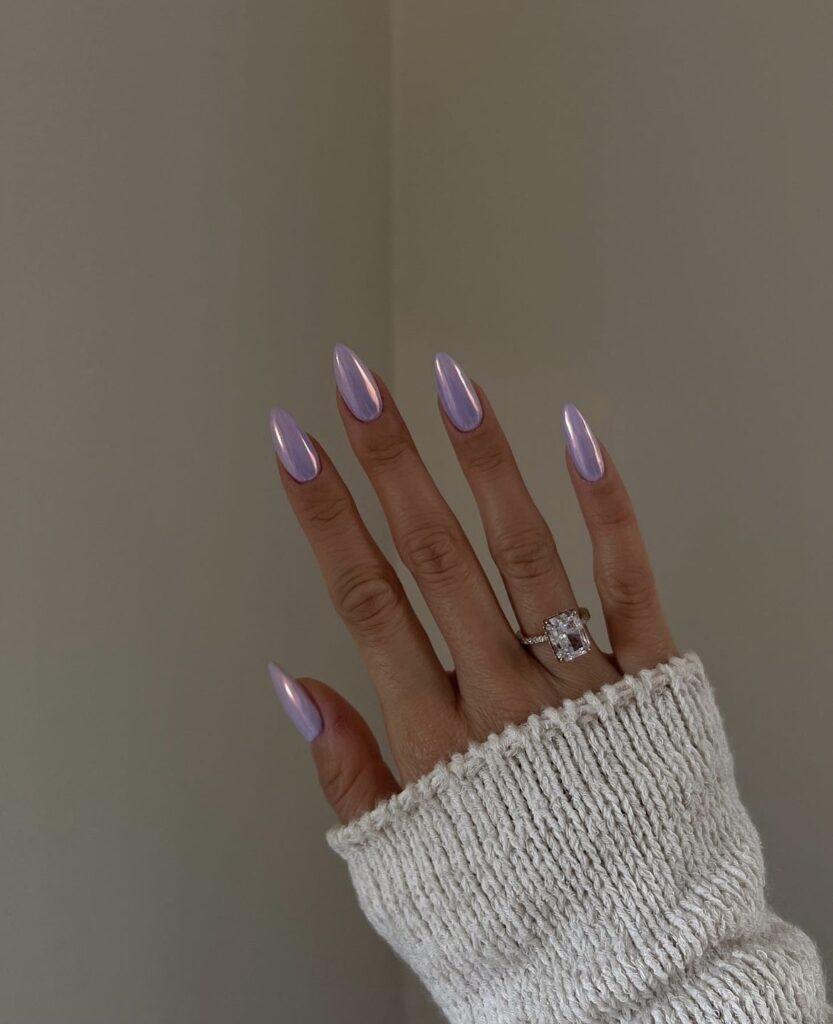 A hand featuring almond-shaped nails with a lavender holographic polish, catching the light for a mesmerizing effect.