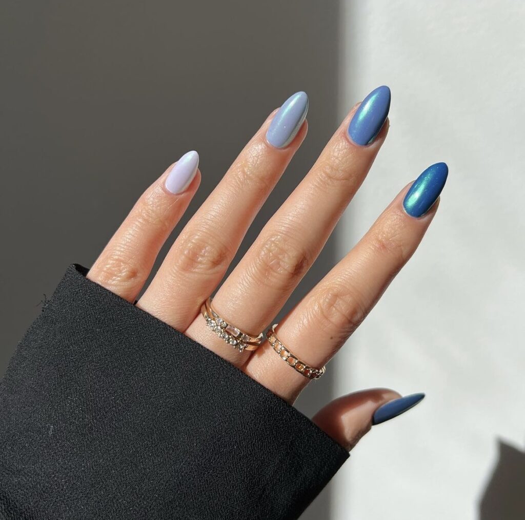 A hand elegantly displays a set of nails with a gradient design, beginning with pale lavender and deepening to a rich sapphire blue, finished with a shimmer.