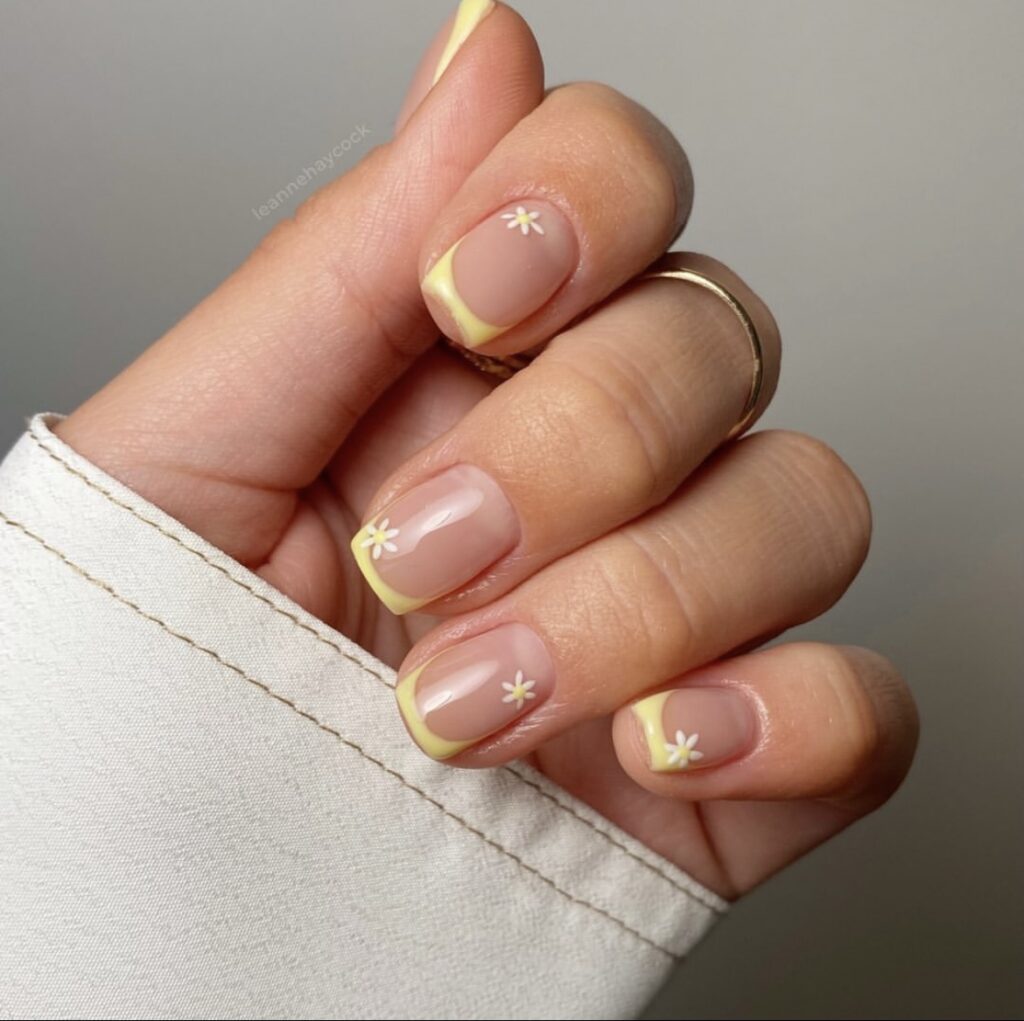 An image showcasing nails with a pale yellow tip and a small white daisy, capturing the simplicity of summer.