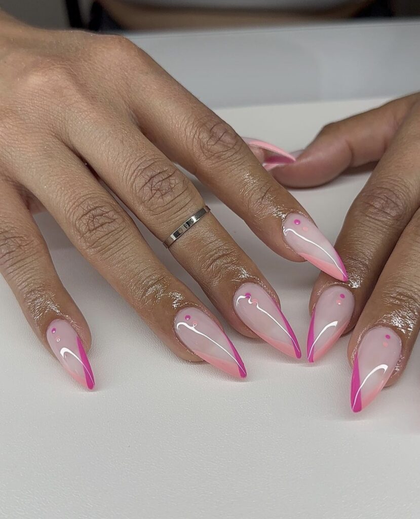A hand with sharp stiletto nails featuring vibrant pink tips and coordinating pink dots, creating a look that's both playful and chic.