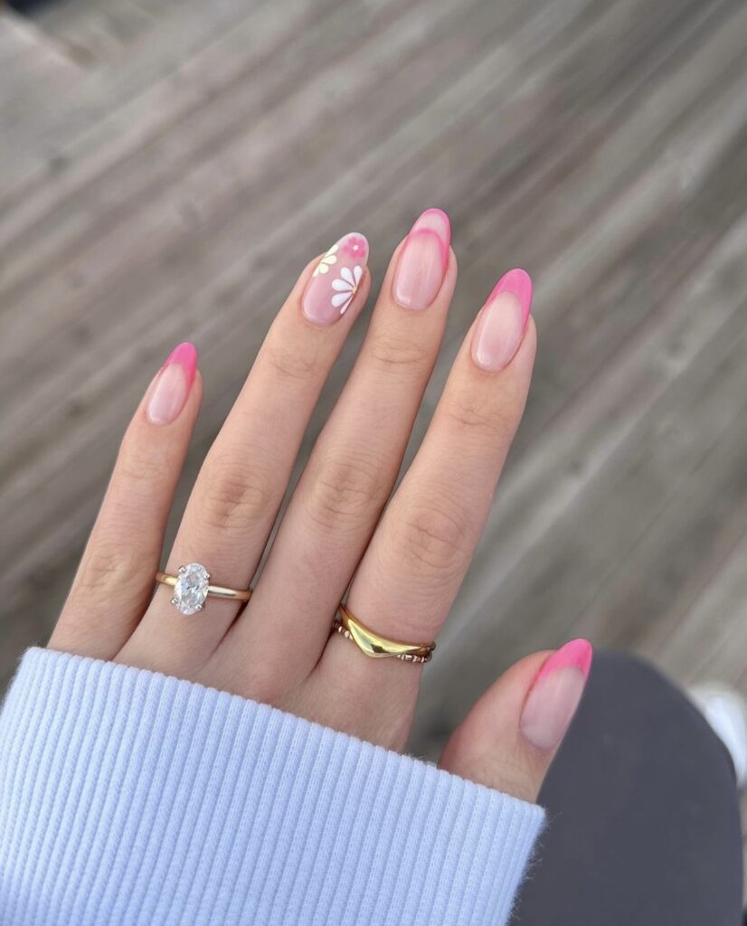  hand is displayed with nails that transition from a translucent pink base to vibrant pink tips, while the ring finger showcases a graceful floral pattern.
