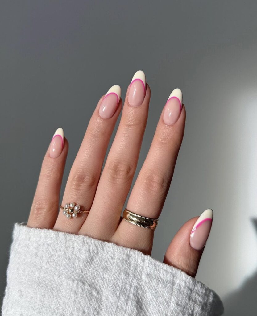 A hand features almond-shaped nails with a delicate yellow tip, accented with a bold pink outline, reminiscent of a colorful summer sunset.