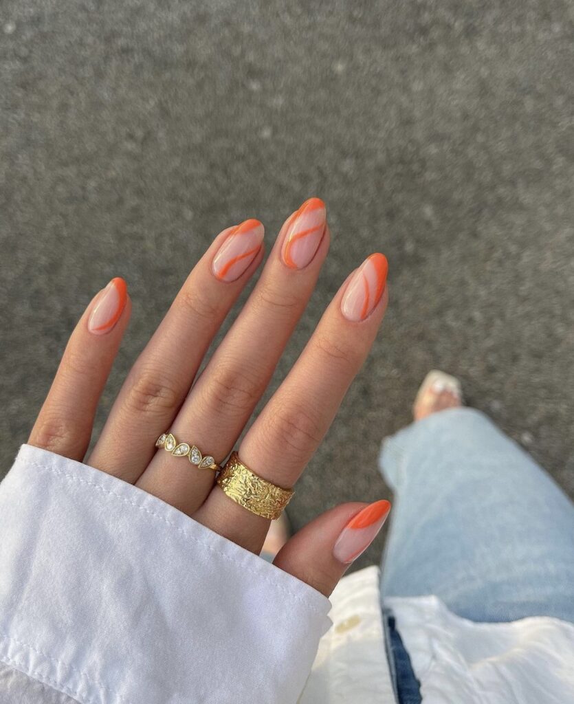 A photo capturing a hand with nails featuring elegant swirls of apricot, set off by stylish gold rings, embodying a breezy summer elegance.