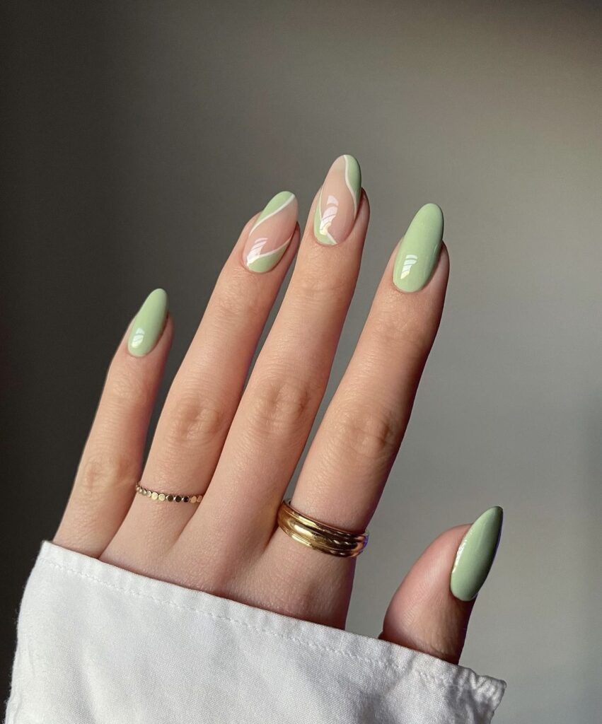 A hand gracefully presents almond-shaped nails painted in a refreshing mint green shade, each adorned with a subtle white artistic detail for an elegant finish.