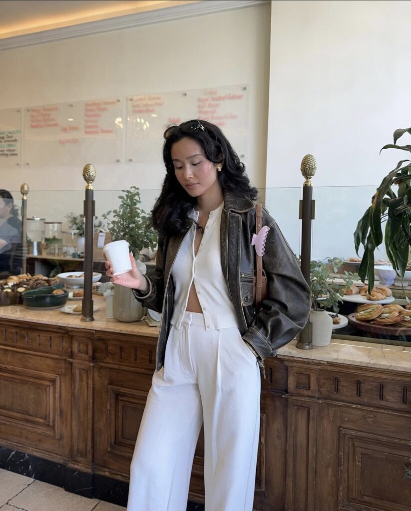 White wide-leg pants are matched with a white cardigan and leather jacket, accessorized with a small handbag and sunglasses. This neutral-toned outfit is perfect for cooler days, providing both warmth and style.