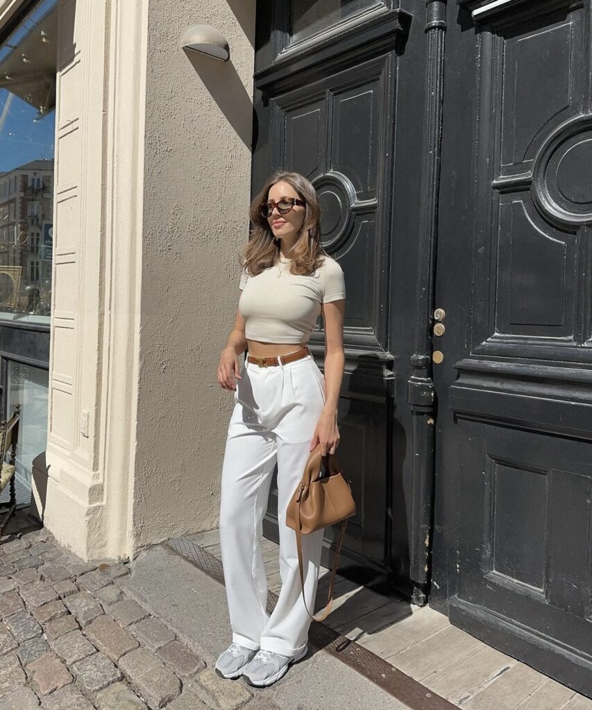 White wide-leg pants paired with a beige crop top, accessorized with a brown belt and handbag. 