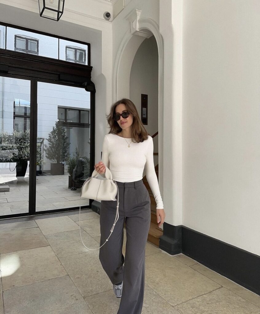 Grey wide-leg pants matched with a white long-sleeve top, accessorized with a white handbag and sunglasses. 