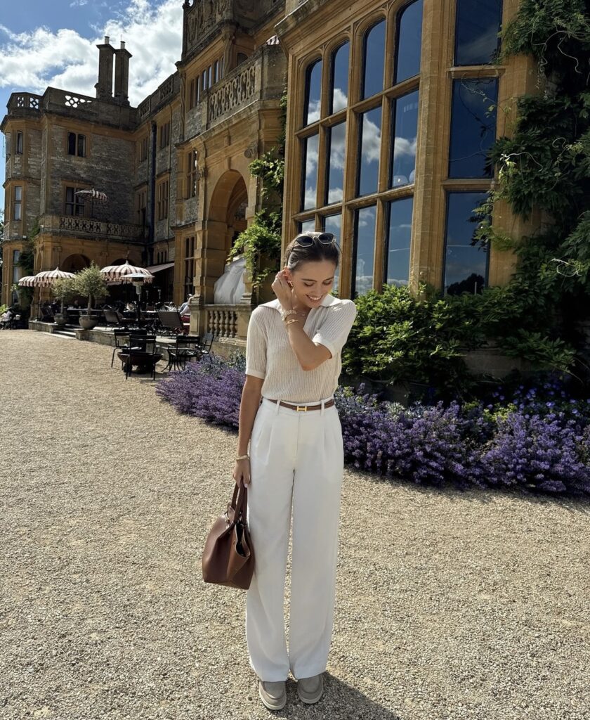 White wide-leg pants paired with a cream beige short-sleeve top, accessorized with a small brown handbag and a brown belt. 