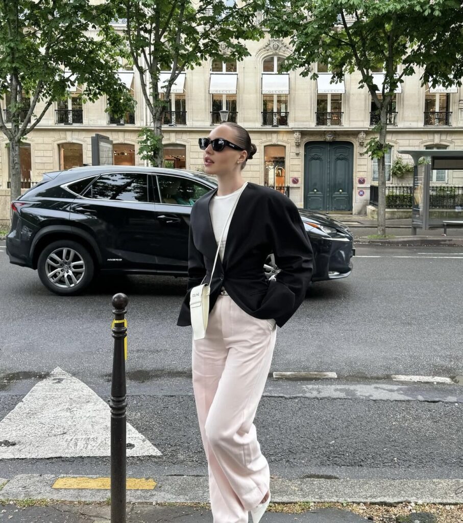 Pale pink wide-leg pants paired with a black blazer and a white tee, accessorized with a small white bag and sleek sunglasses.