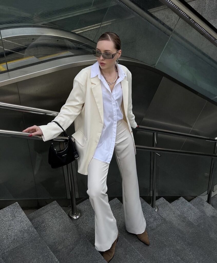 White wide-leg pants paired with a white button-down shirt and a long white coat. The look is finished with a brown handbag and neutral shoes, creating a stylish outfit for a cool day.