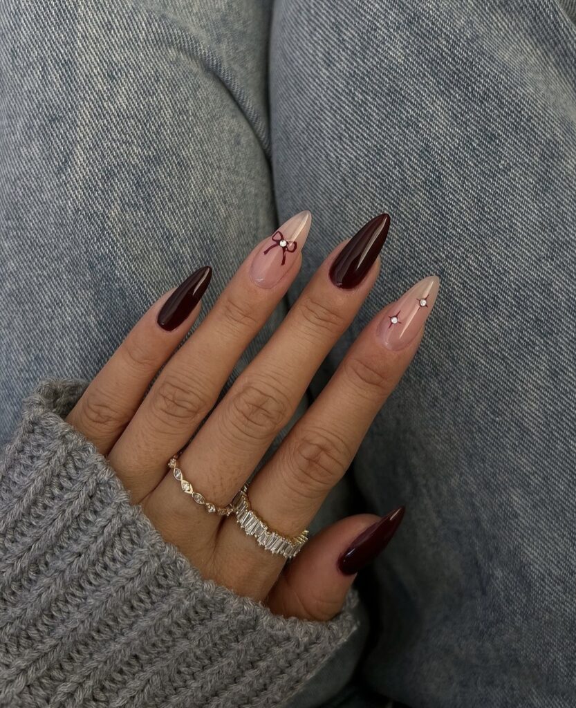 Burgundy nails with delicate bow accents on the ring finger and neutral nails.