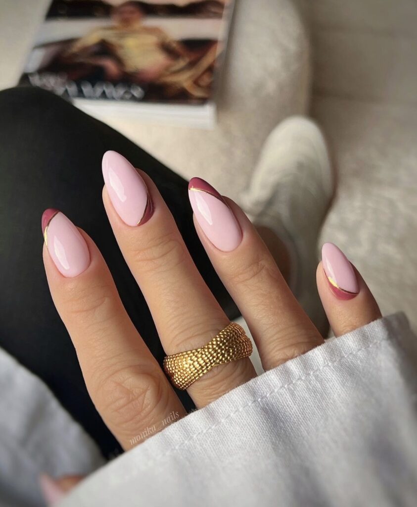 Light pink nails with diagonal burgundy tips and gold accent lines.