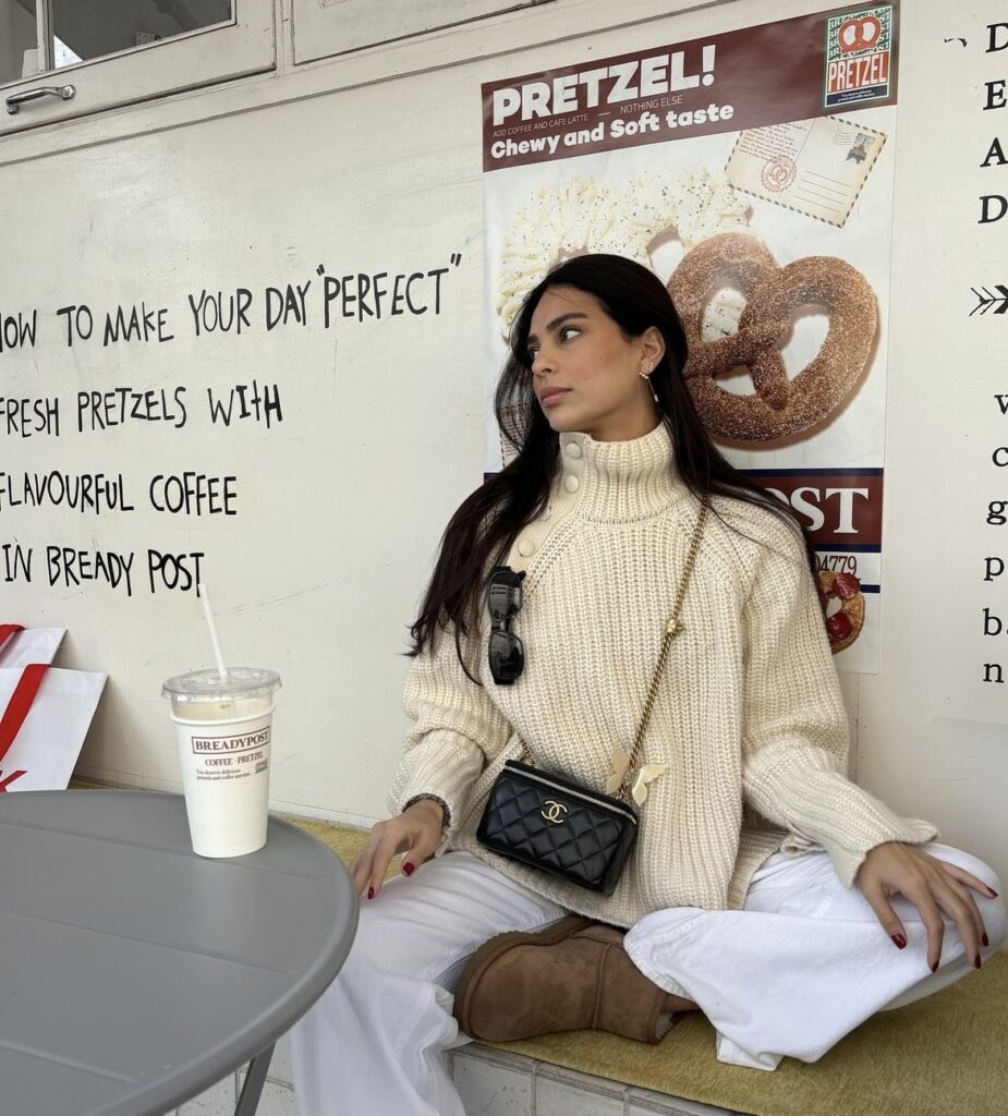 A knit sweater paired with white trousers and a black crossbody bag.