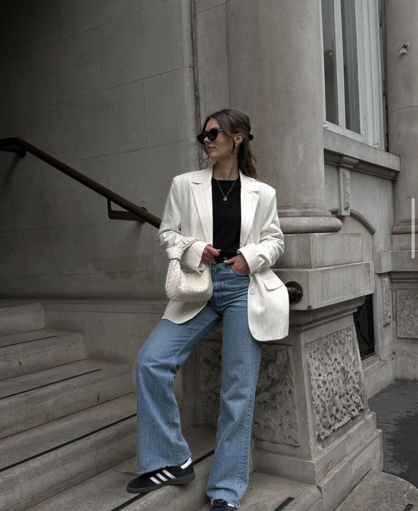 A balanced casual-formal outfit with a blazer, light wash jeans, a classic black top, and stylish sneakers.