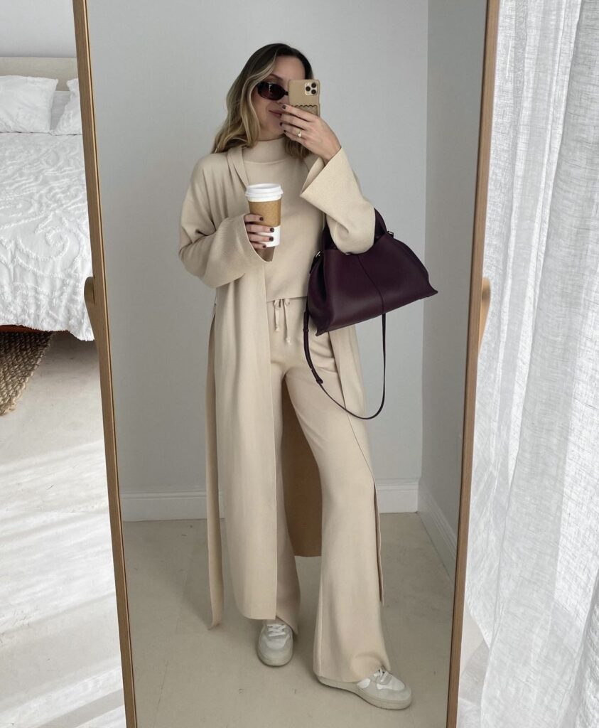 A beige cardigan and wide-leg trousers, styled with a handbag and sneakers.