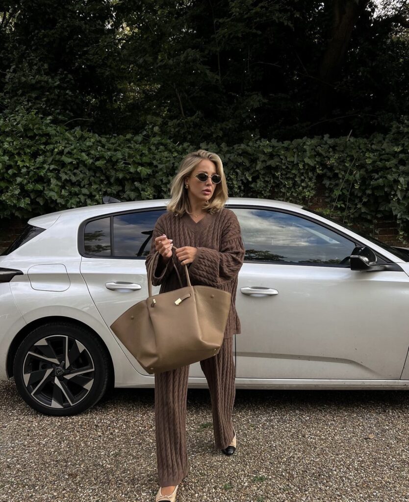 A rich brown knitted set, with a matching top and trousers, tote bag, and chic sunglasses for a warm and stylish travel look.