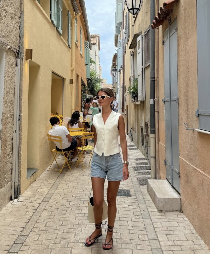 Woman in a sleeveless vest and denim shorts with strappy sandals and a tote bag, perfect for a casual day out.