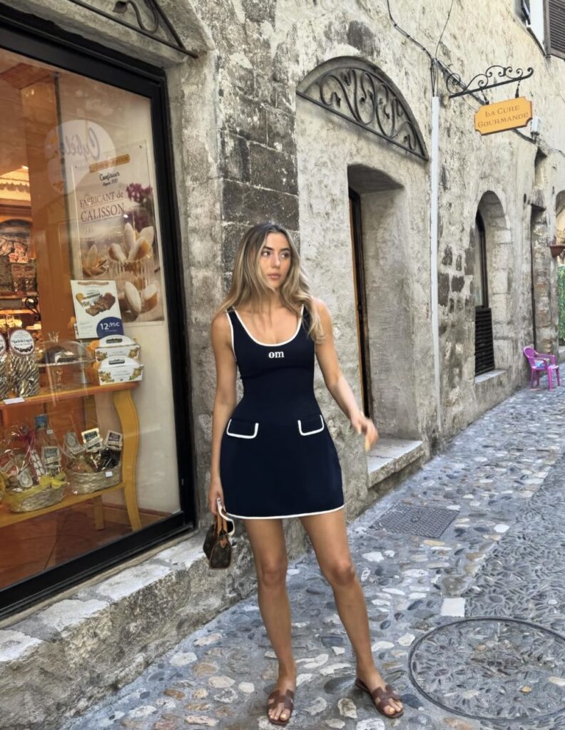 Woman wearing a navy mini dress with white trim and brown sandals.