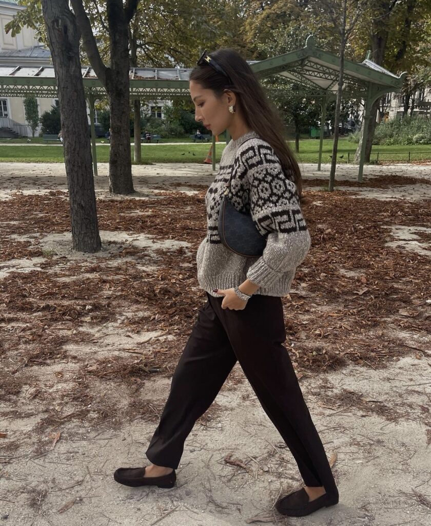 Woman wearing black pants with a patterned sweater and loafers.