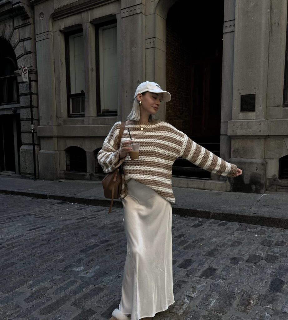 Woman wearing a cozy sweater with a satin maxi skirt and sneakers.