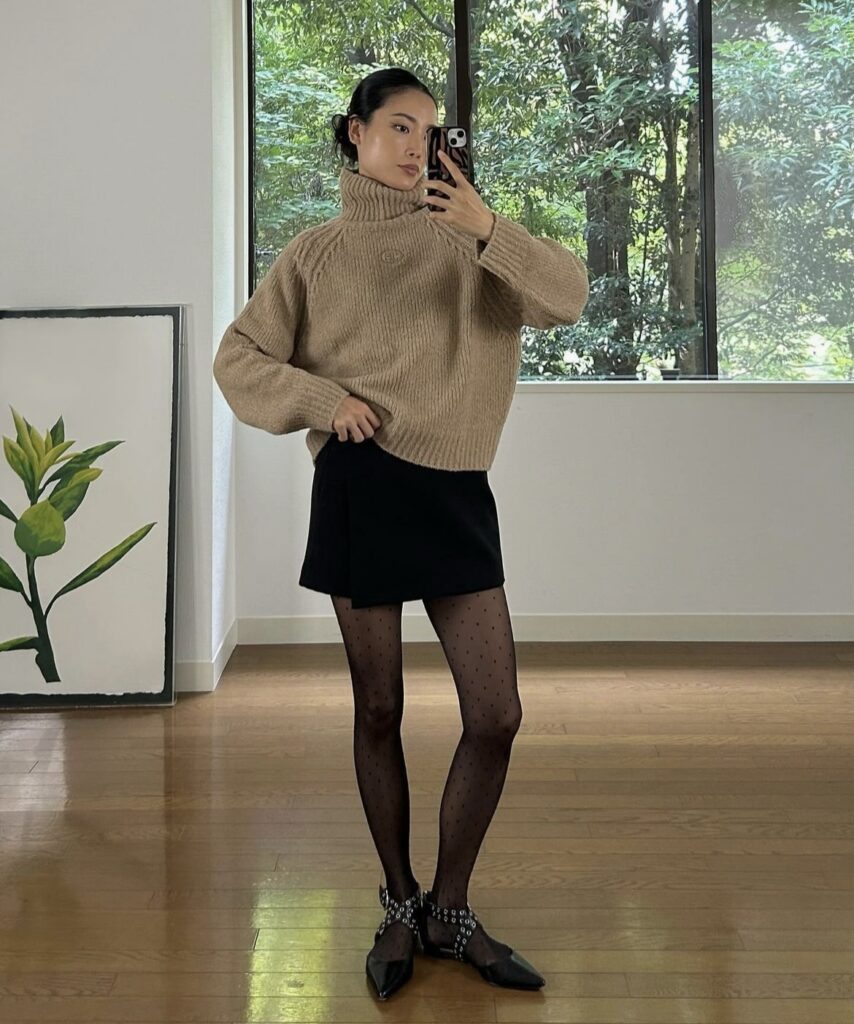 Woman wearing a turtleneck sweater with a mini skirt and polka dot tights.