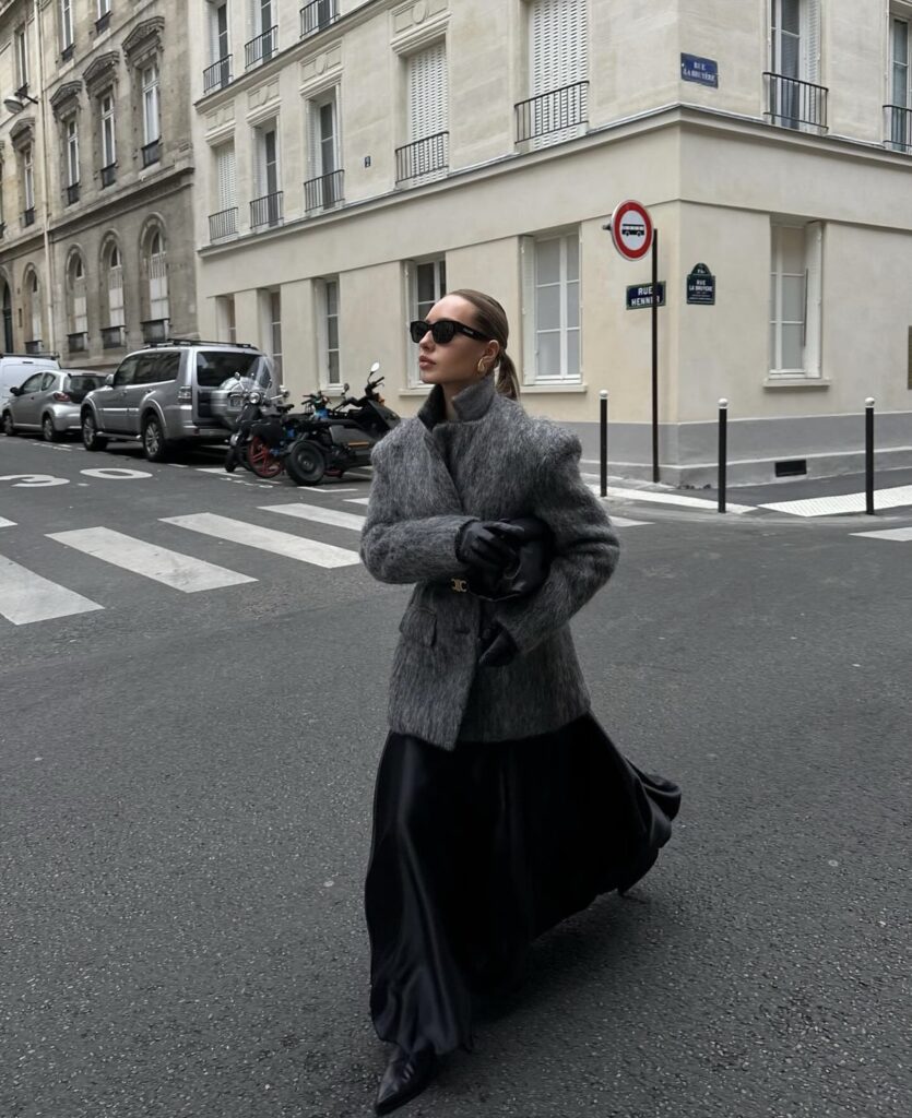 A grey coat layered over a satin skirt, completed with boots and leather gloves.