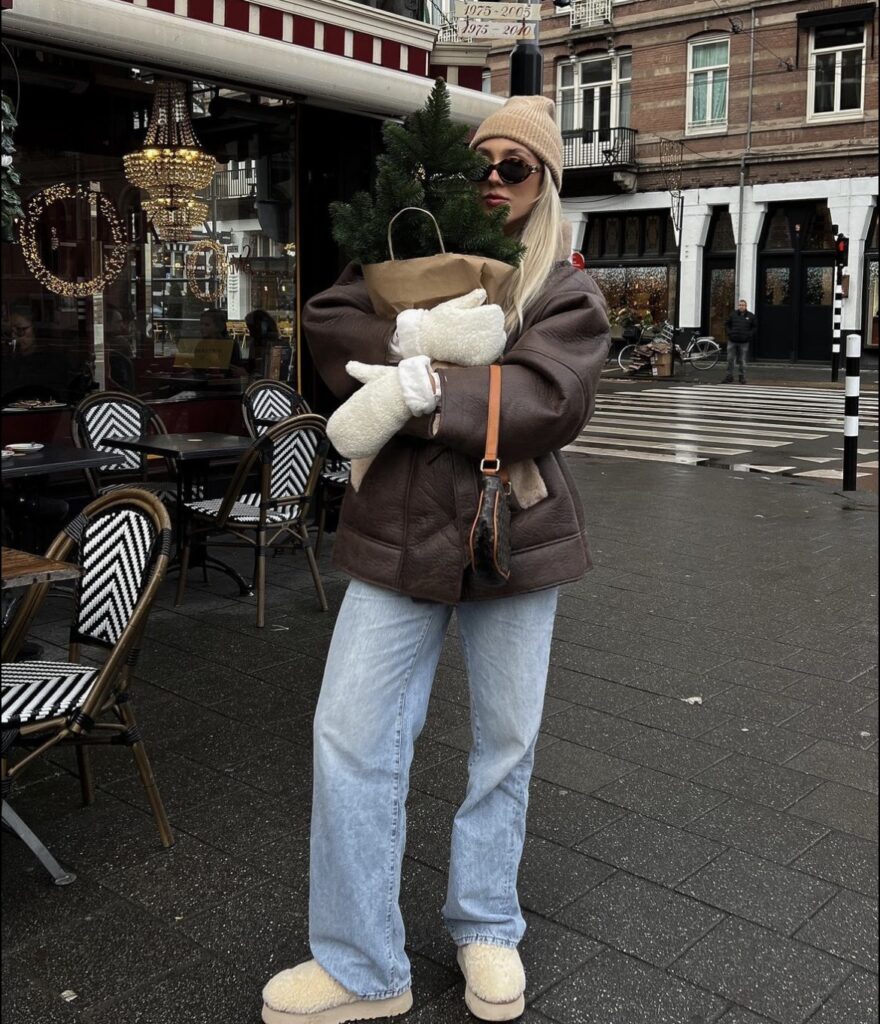 A brown leather jacket with light-wash jeans, mittens, and a beanie.