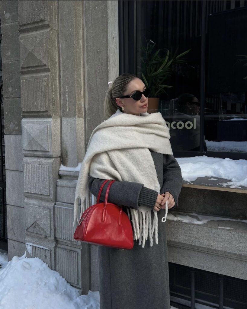 A white scarf with a grey coat, a red handbag, and stylish accessories.