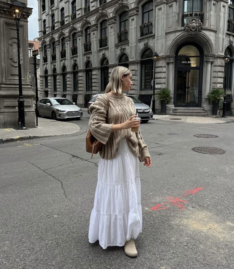 A beige knit sweater with a flowing white maxi skirt and elegant accessories.