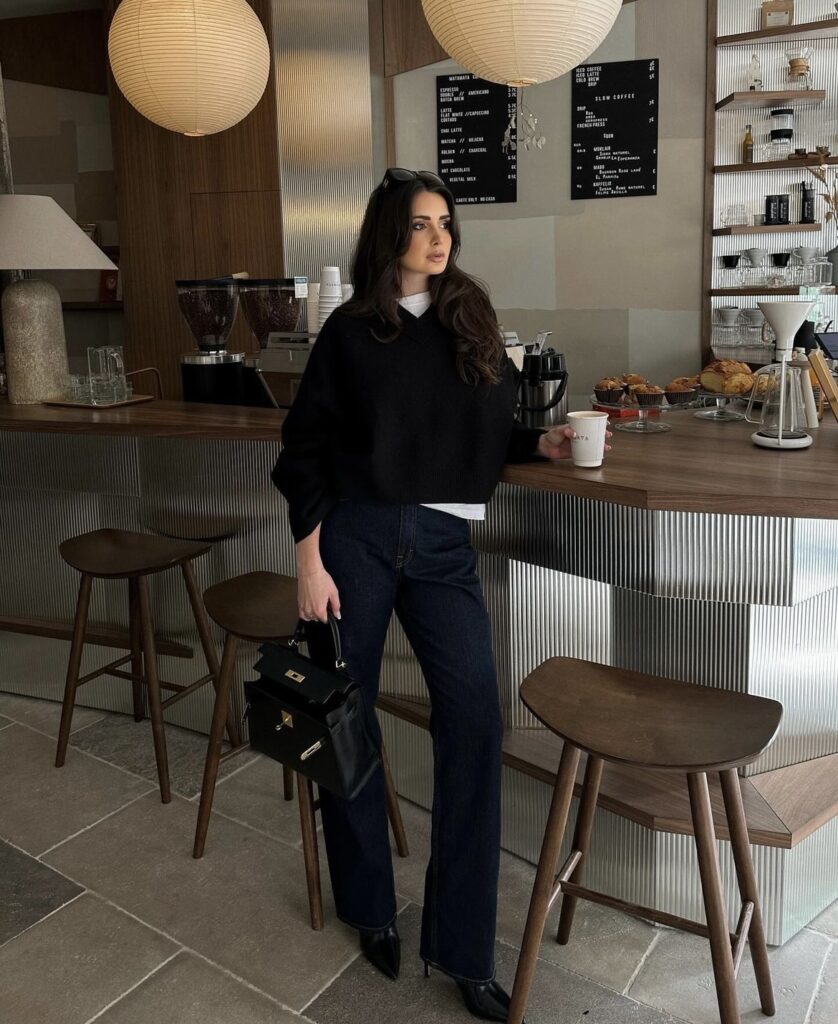 A relaxed winter outfit, pairing black boots with dark wash jeans and a cropped black sweater.