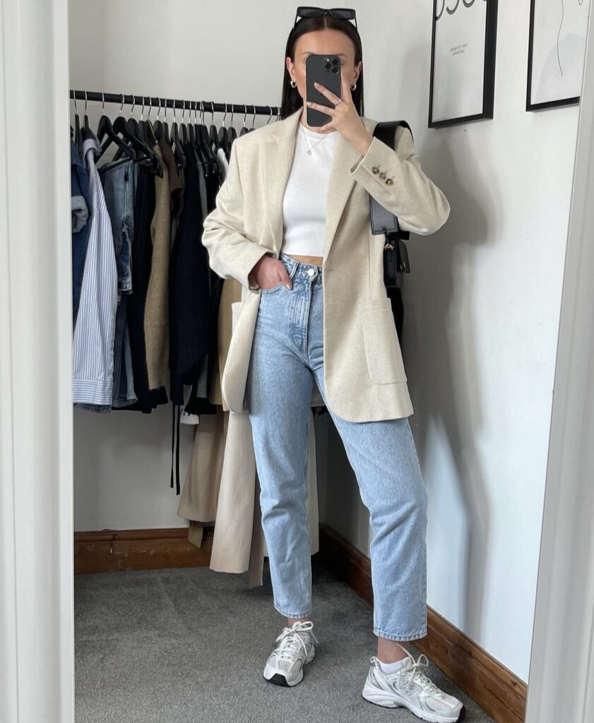 A mirror selfie of a person wearing a light beige blazer over a white crop top, paired with high-waisted light blue jeans and white sneakers.