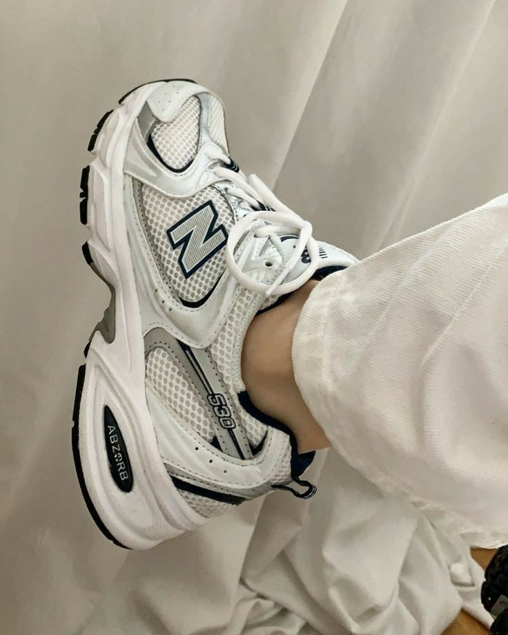 A close-up of a foot wearing New Balance 530 sneakers, paired with white pants. The detailed design of the sneaker, including the ABZORB midsole, is prominently visible.